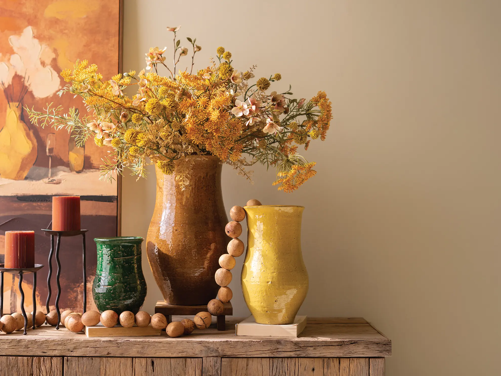 Fall vignette with ceramic vases, wooden garland, iron candlestands, and botanica bouquet.